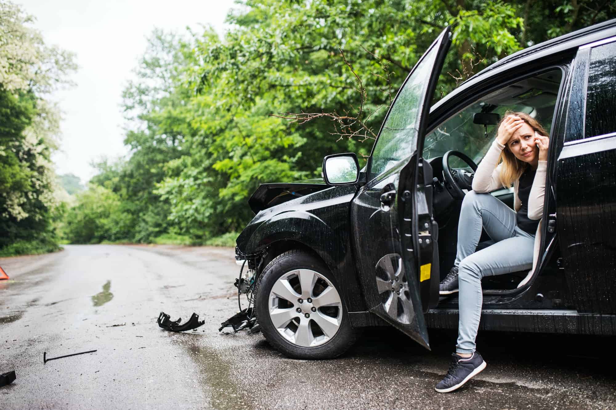 Young woman in the damaged car after a car accident, making a phone call.